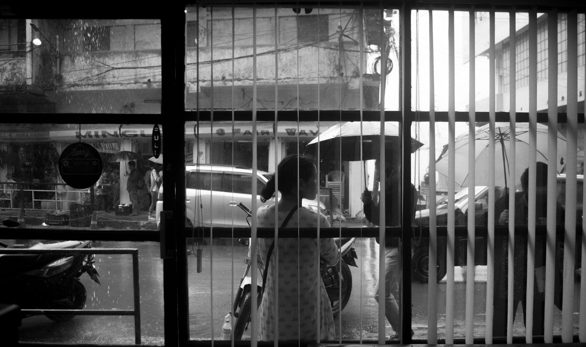 A black and white street view captured through a window on a rainy day.