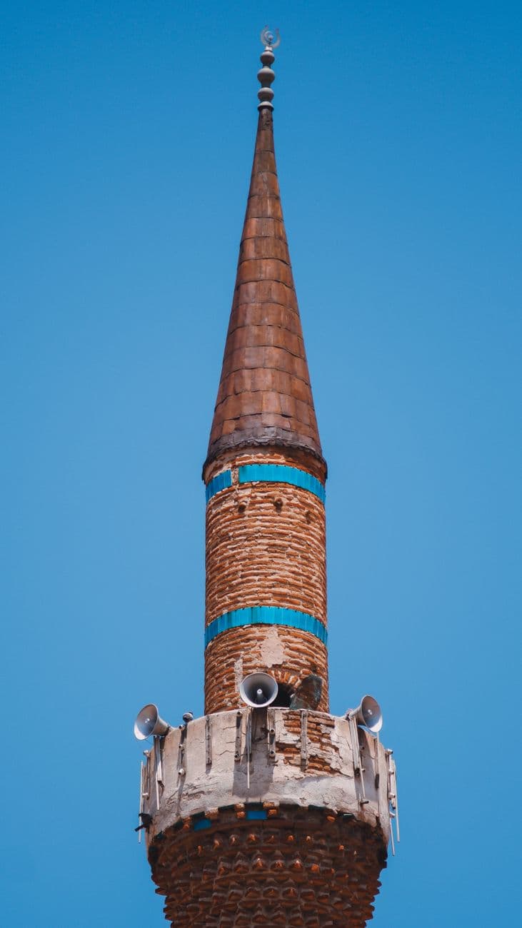 A brown brick minaret adorned with speakers against a clear blue sky.