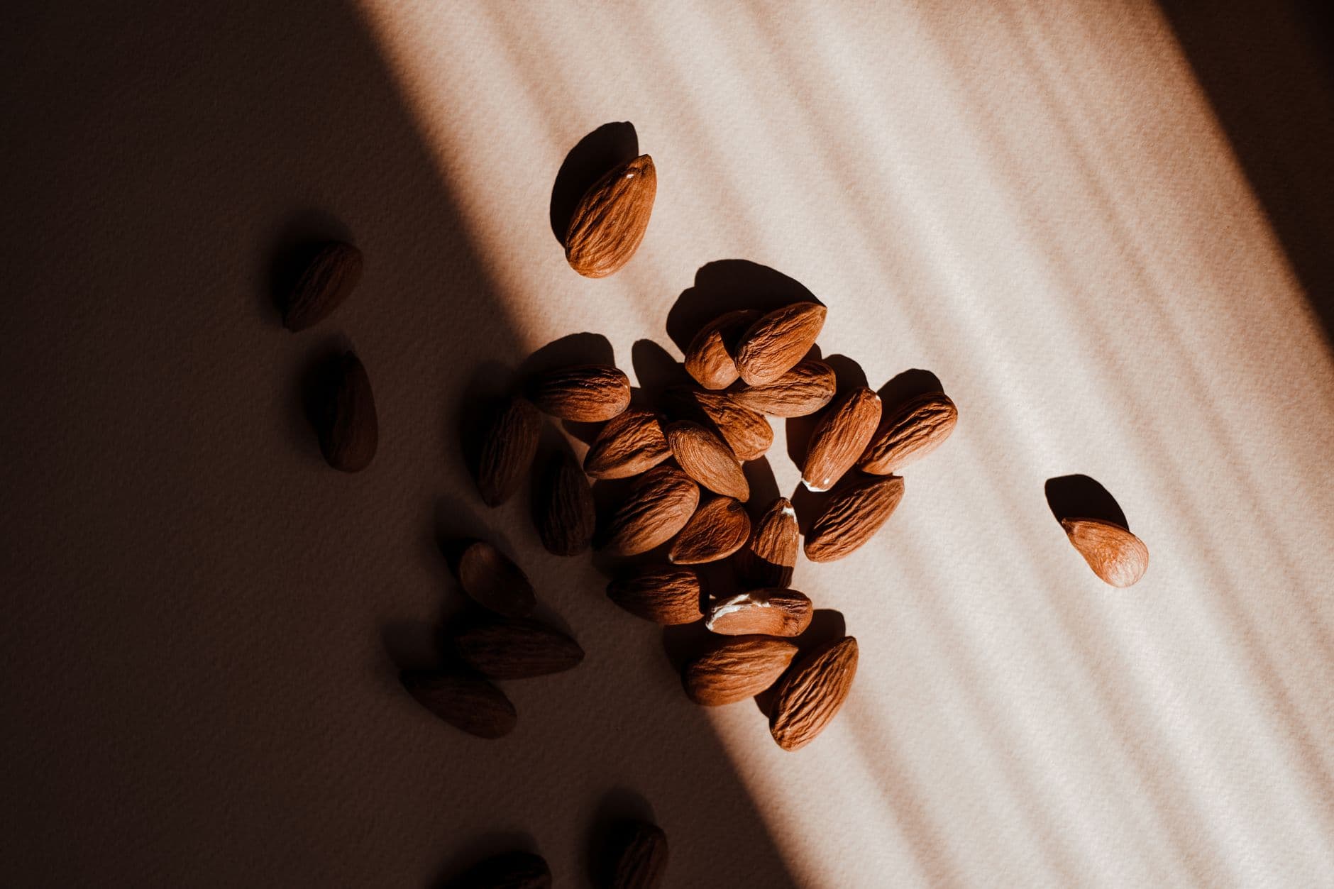 A close-up of almonds highlighted by sunlit shadows on a neutral surface.