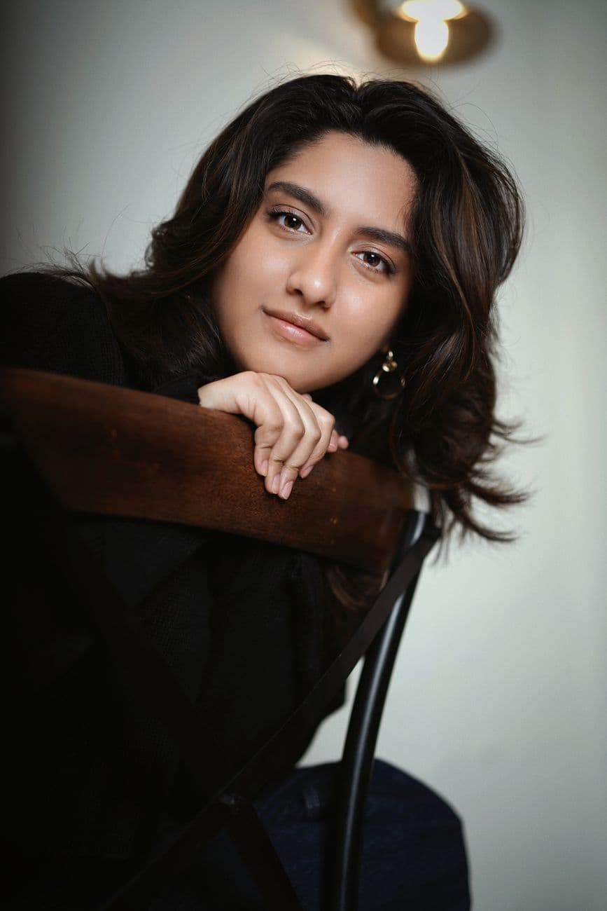 A close-up portrait of a young woman leaning on a chair indoors.