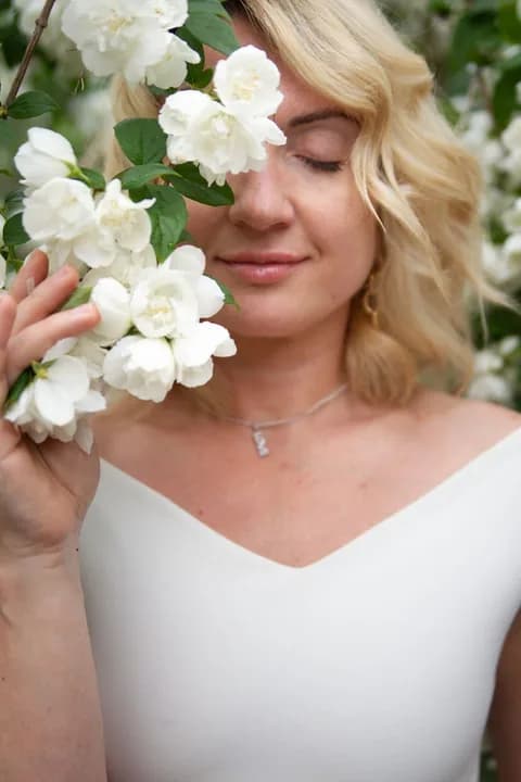 A serene portrait of a blonde woman enjoying white blossoms outdoors. PNG