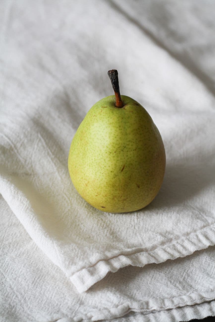 A single fresh green pear resting on a soft white cloth background.