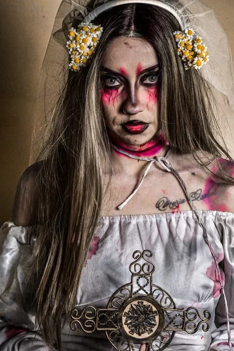 A woman in a haunting bridal costume holding an ornate cross. PNG