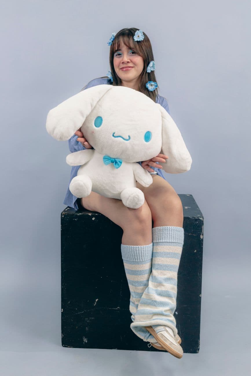 A young woman sits with a large plush toy wearing cozy leg warmers.