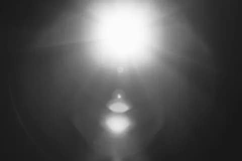 Abstract black and white image of a bright sun flare with lens effects. PNG
