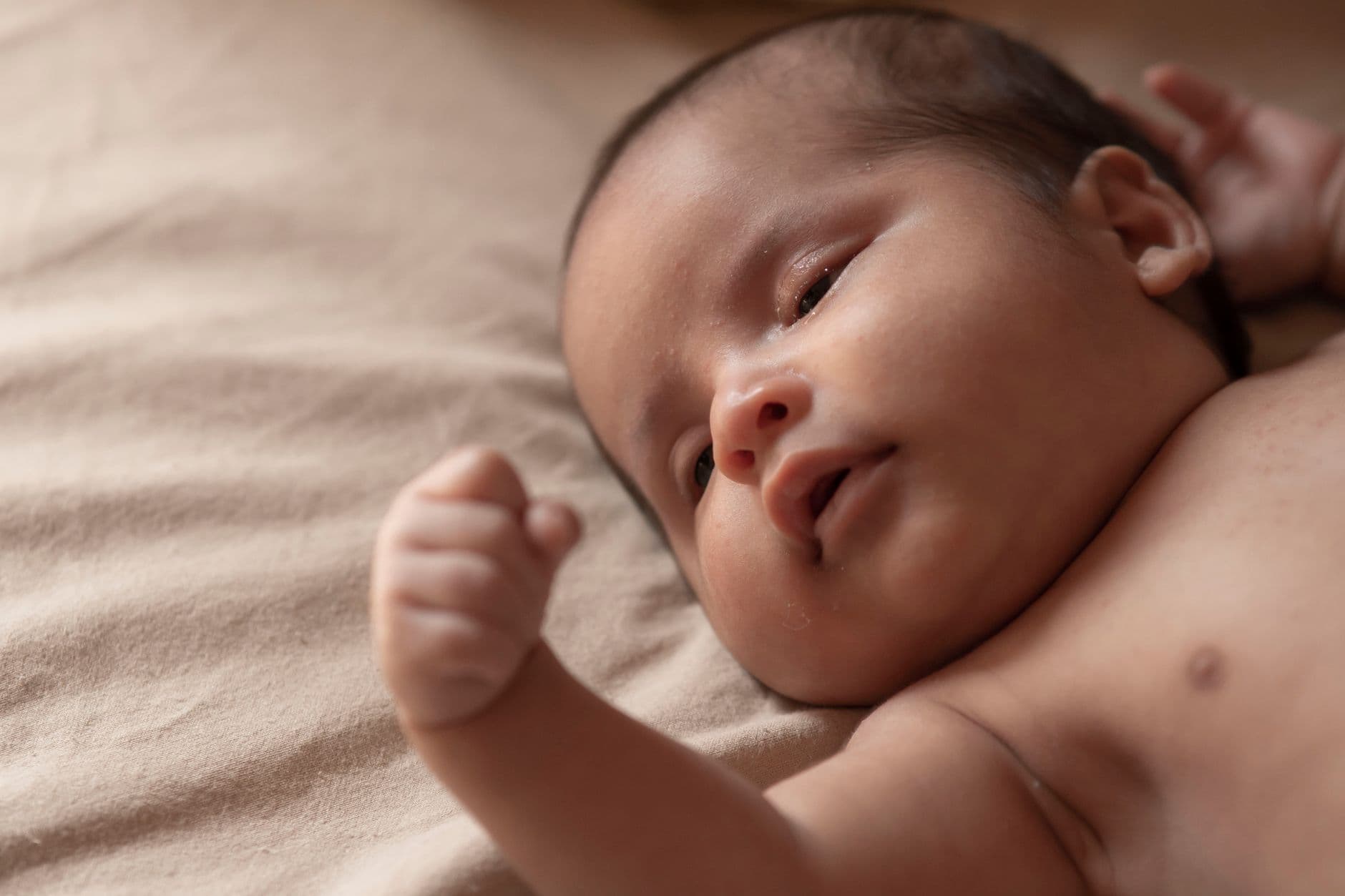 Adorable baby lying on a soft beige blanket in natural light.