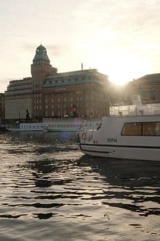 Calm waterfront scene with sunset and boats near historic buildings. PNG