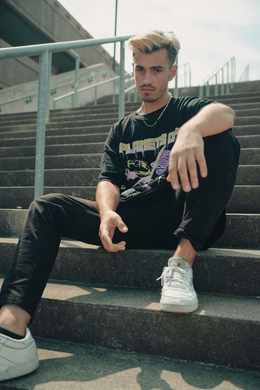 Casually dressed man seated on outdoor concrete stairs on a sunny day.