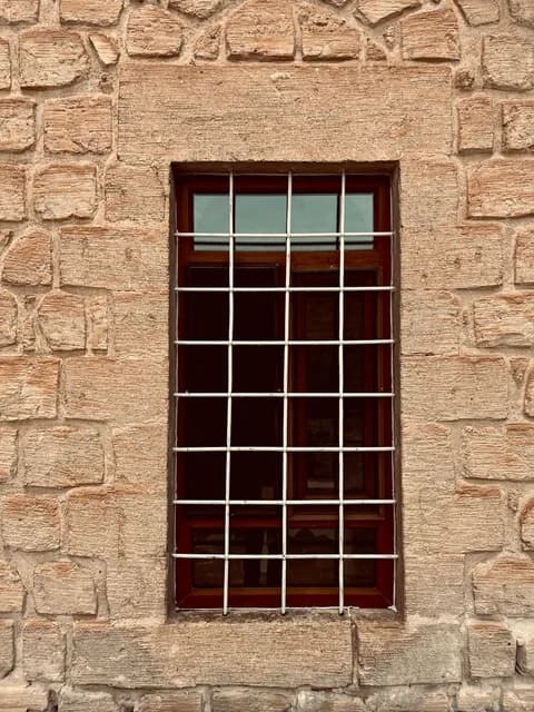 Close-up of a barred window set in a textured stone wall. PNG