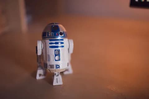 Detailed shot of R2-D2 toy figure on a warm-toned wooden surface. PNG