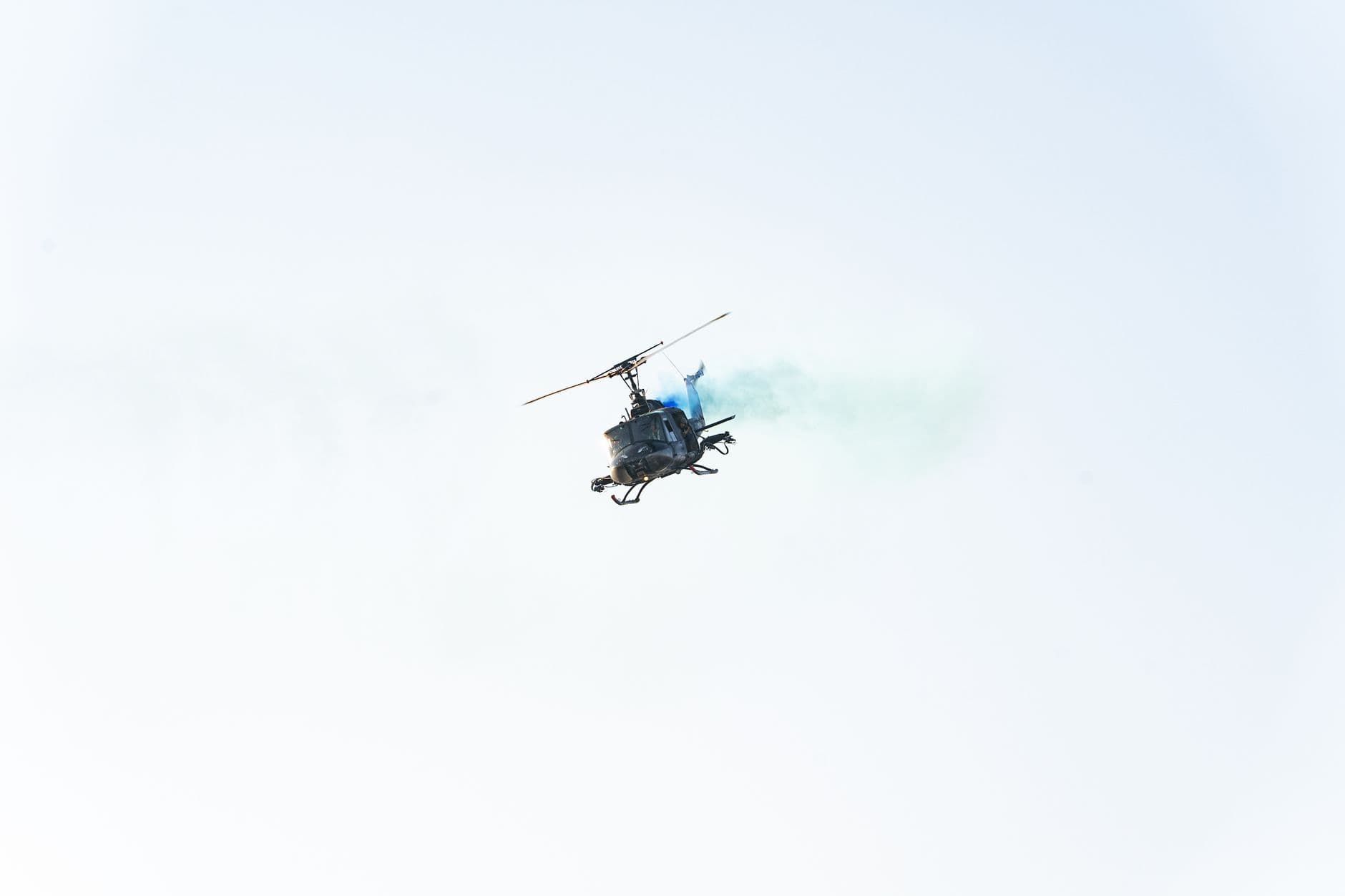 High-altitude helicopter emitting blue smoke in clear El Salvador sky.