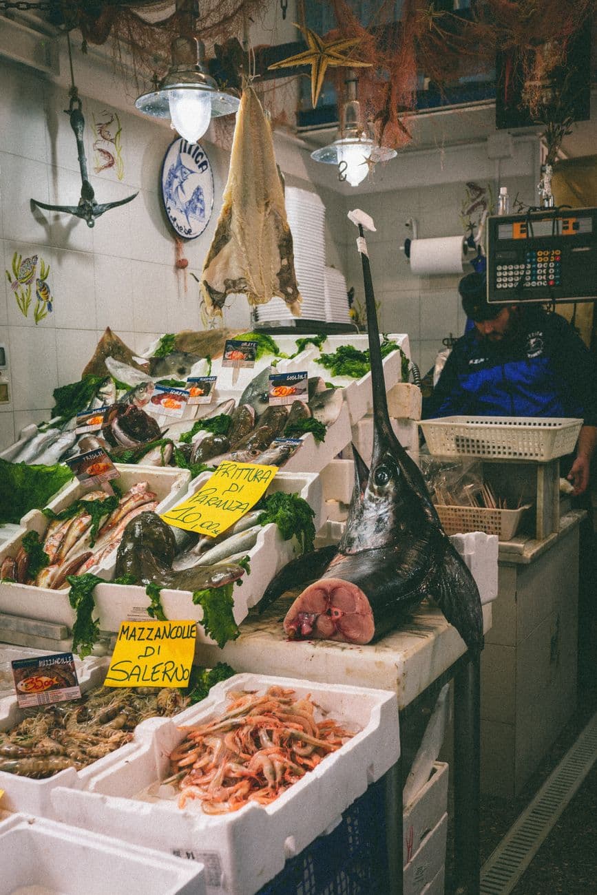 Italian seafood market stall featuring fresh fish, swordfish, and prawns.