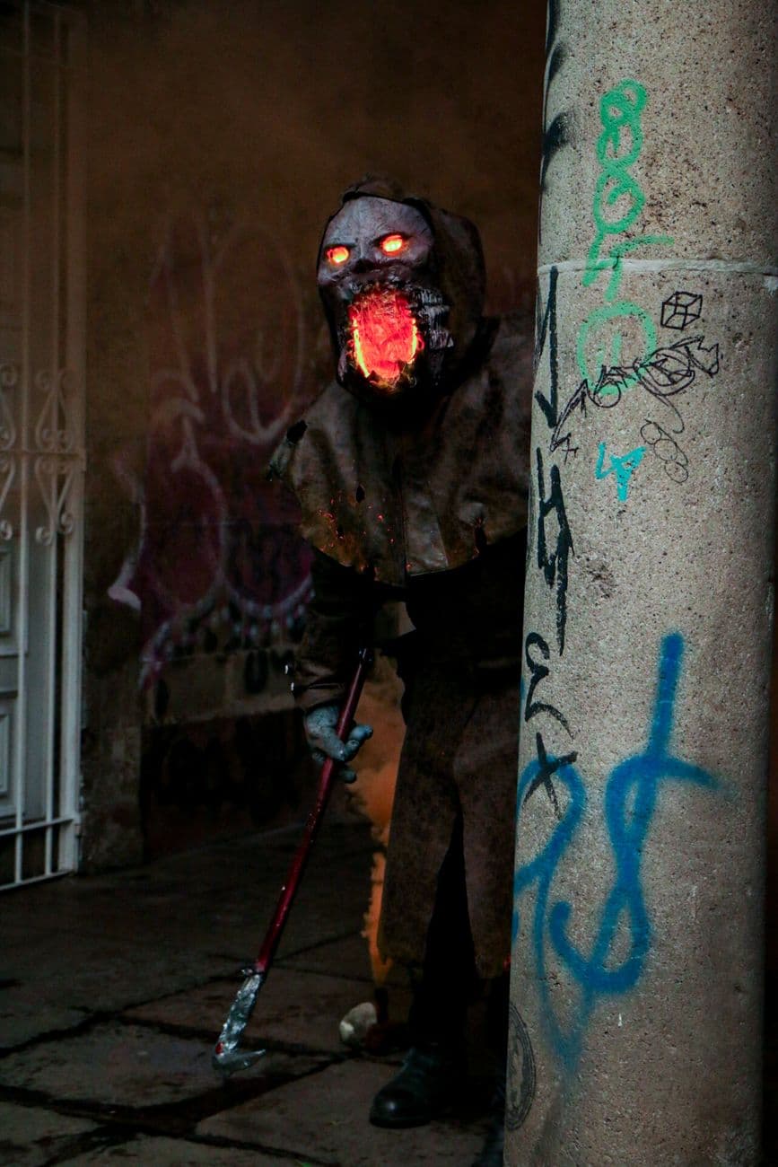Mysterious cloaked figure with glowing face in graffiti-filled alley at night.