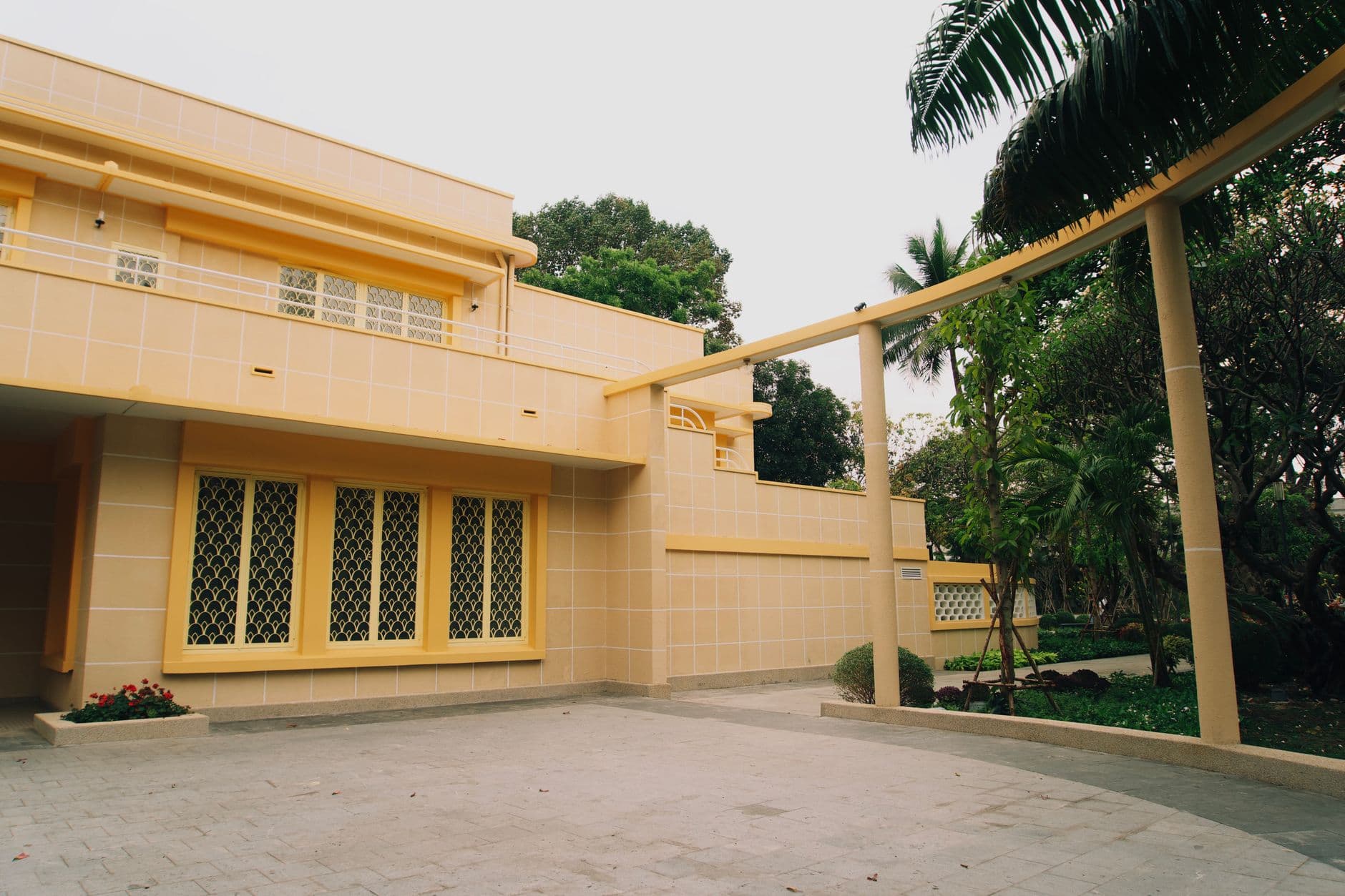 Stylish yellow house with garden, palm trees, and open driveway.