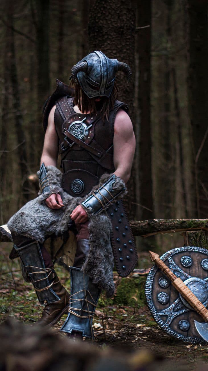 Viking warrior sitting on log in forest, wearing Nordic armor and helmet.