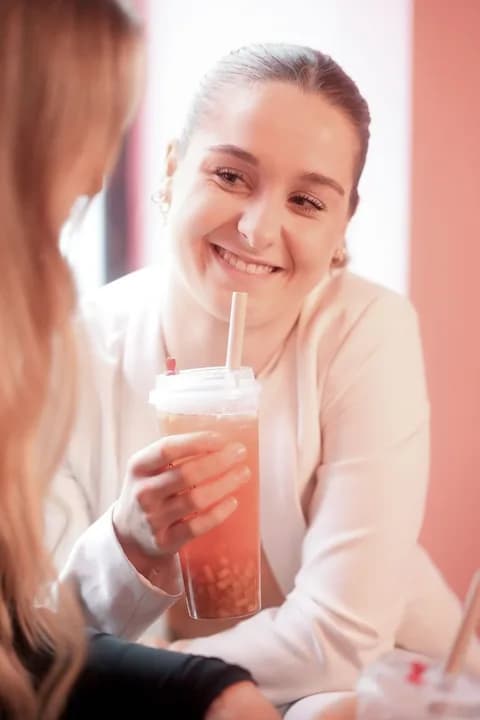 Woman smiling while holding a cup of bubble tea inside a bright café. PNG