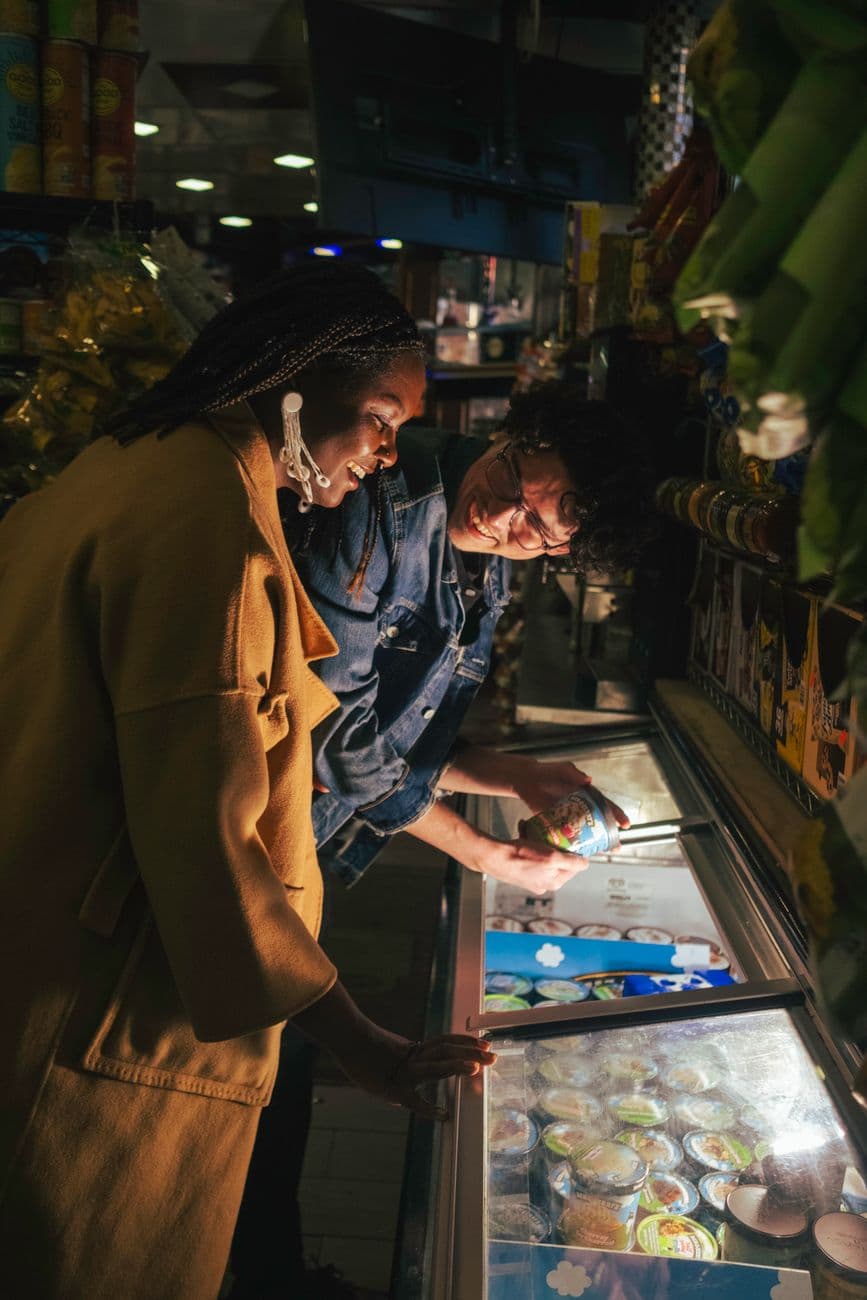 A couple choosing ice cream from a freezer in a dimly lit store at night, smiling and enjo