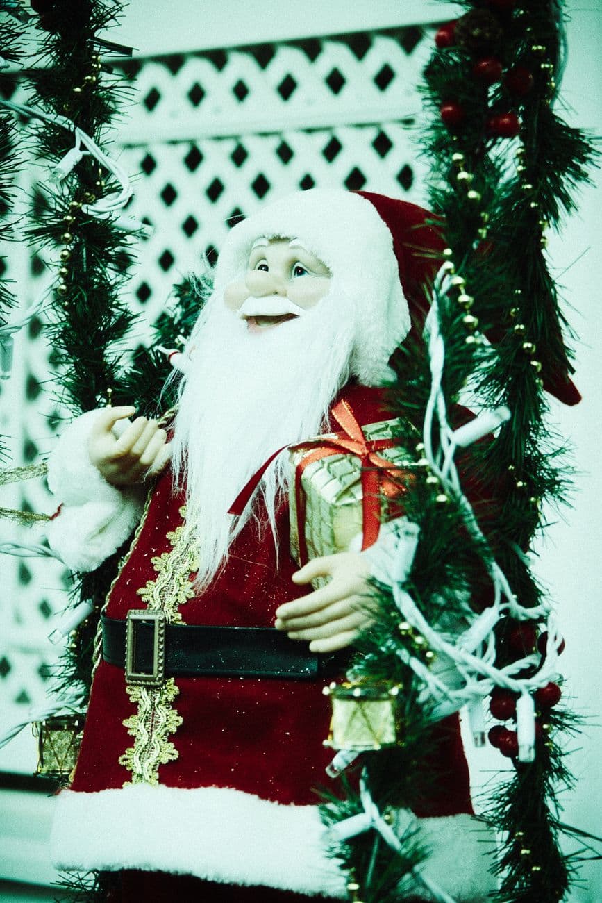 A decorative Santa Claus figure amidst Christmas greenery and gifts for holiday decor.