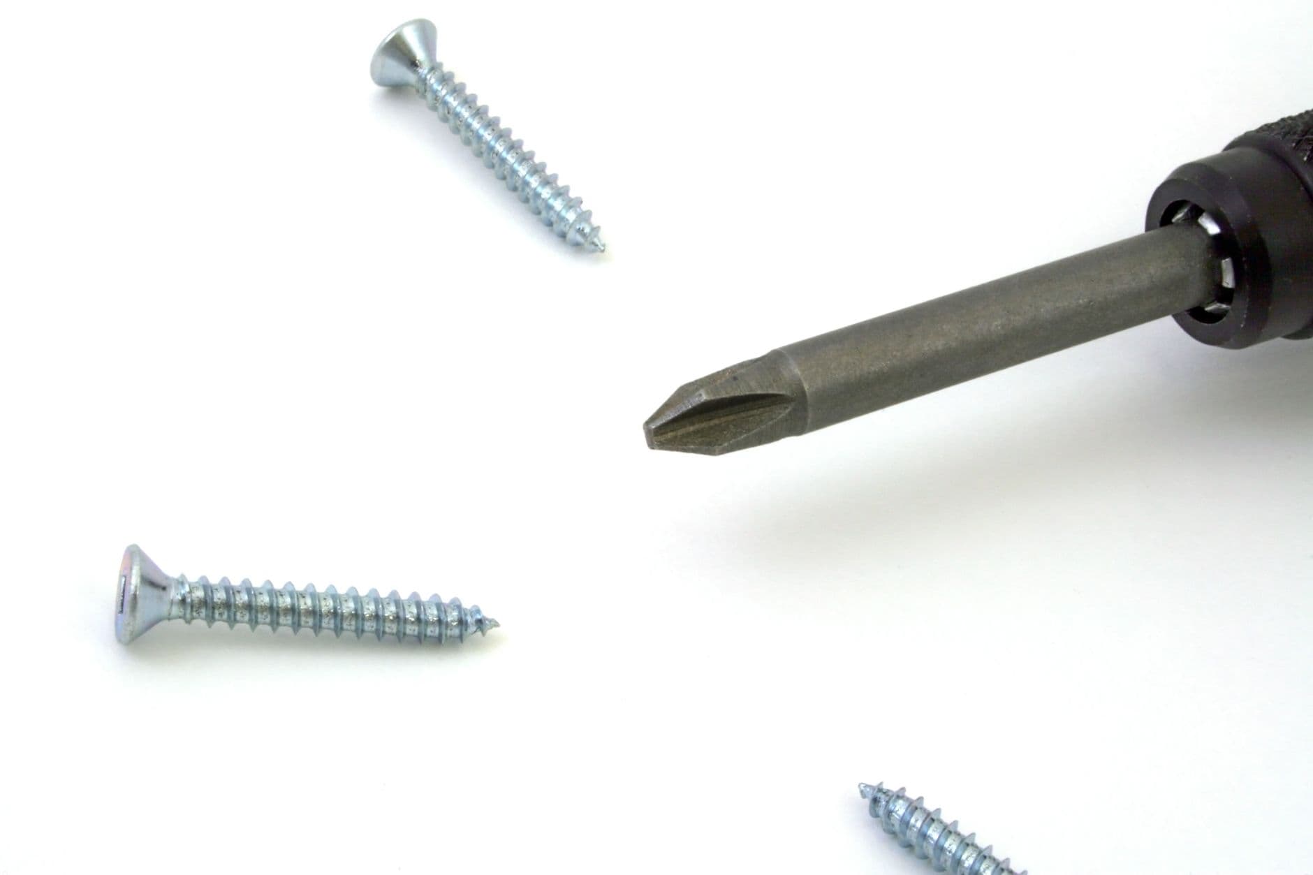 A detailed view of a screwdriver with screws scattered on a white surface, ideal for tool