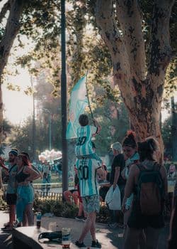 A father carries his son on shoulders waving a flag at an outdoor city celebration. PNG