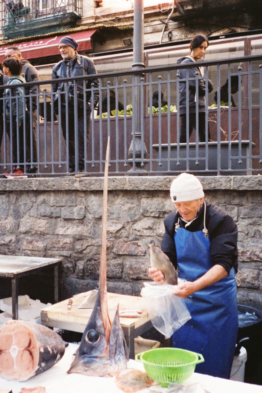 A fishmonger prepares swordfish at a Sicilian market, showcasing local culture.