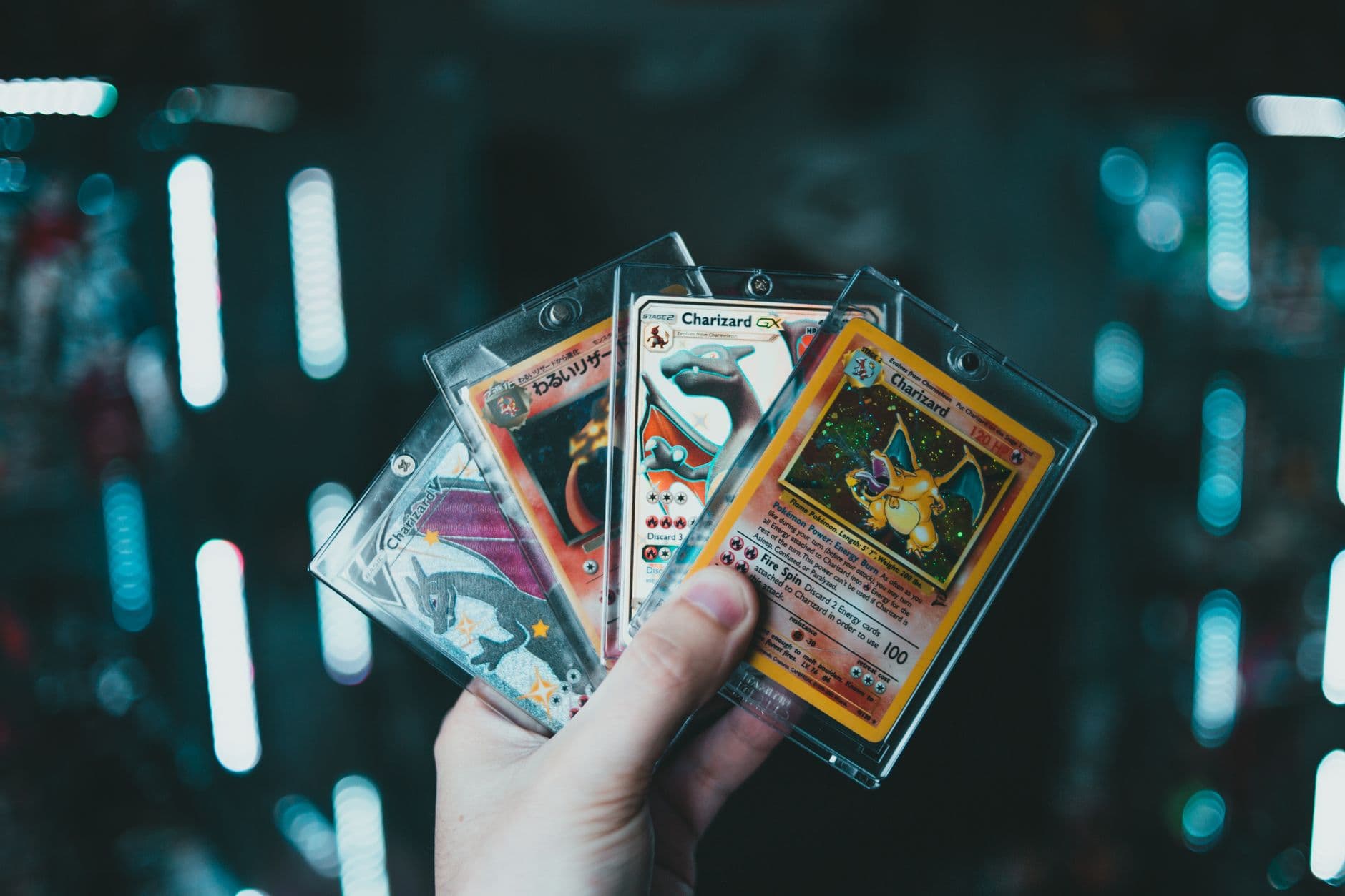 A hand holds collectible Charizard Pokemon cards with a blurred bokeh background. Perfect