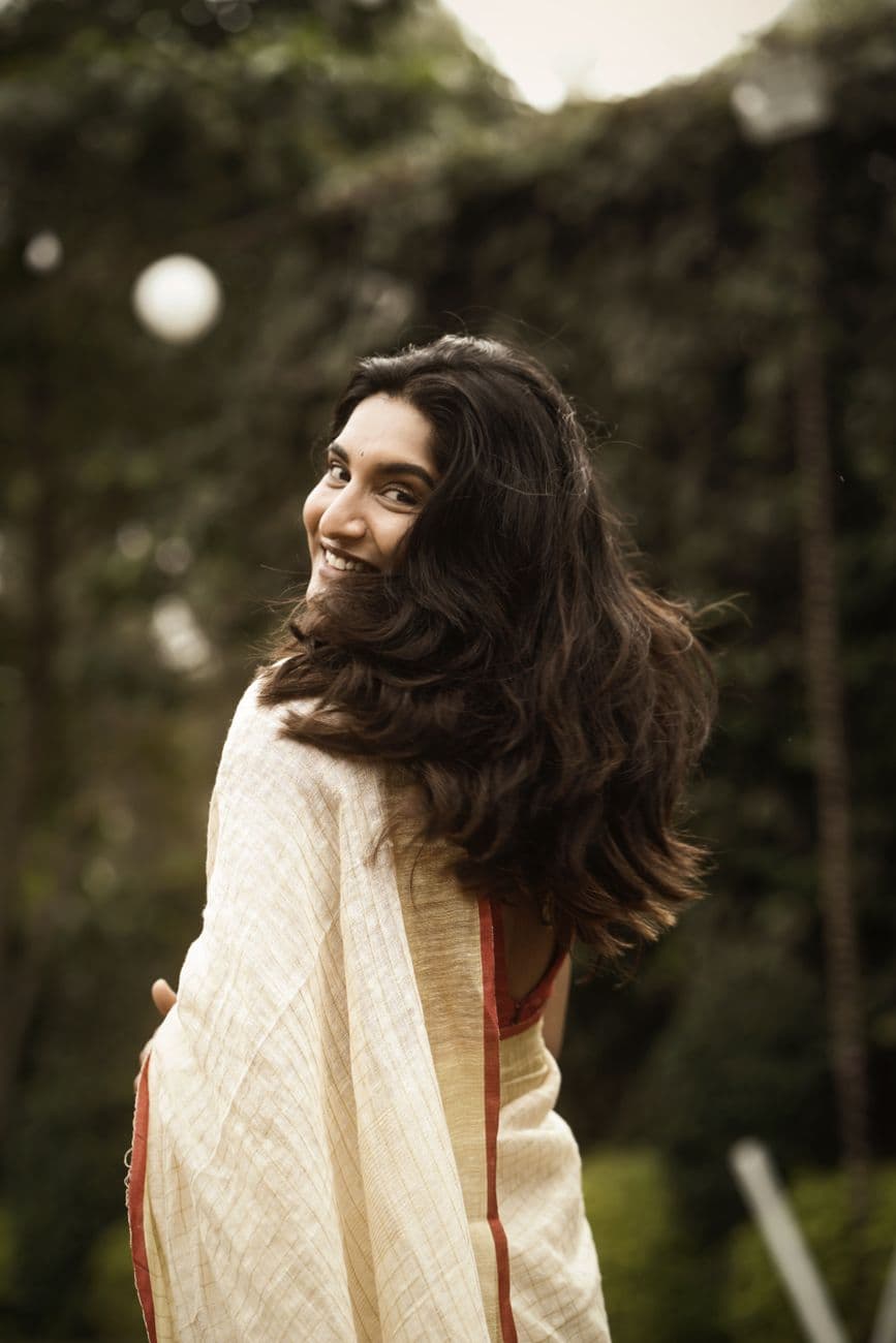 A joyful woman in a traditional white saree laughing outdoors, embracing nature.