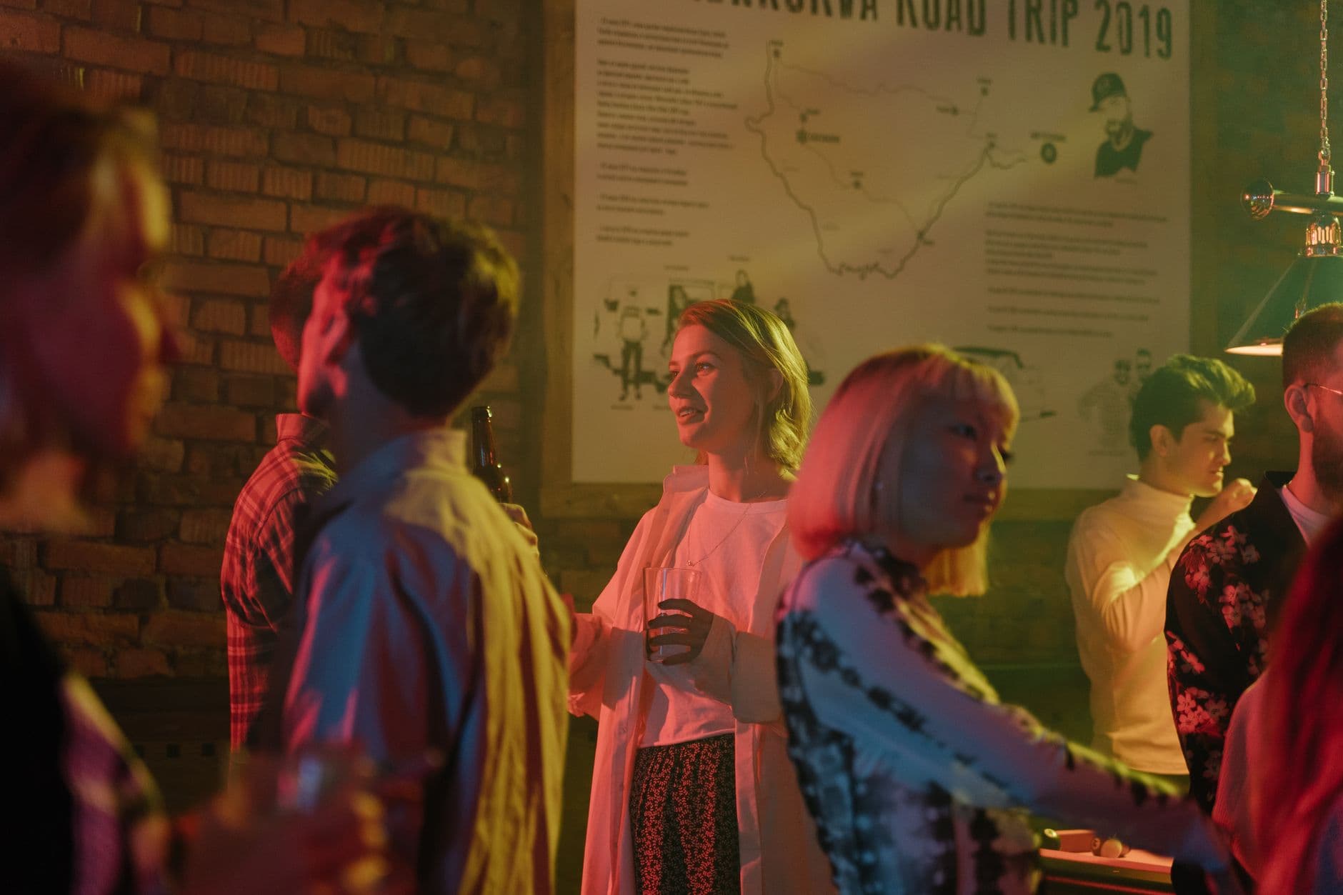A lively indoor party with people socializing in a colorful and dimly lit bar.