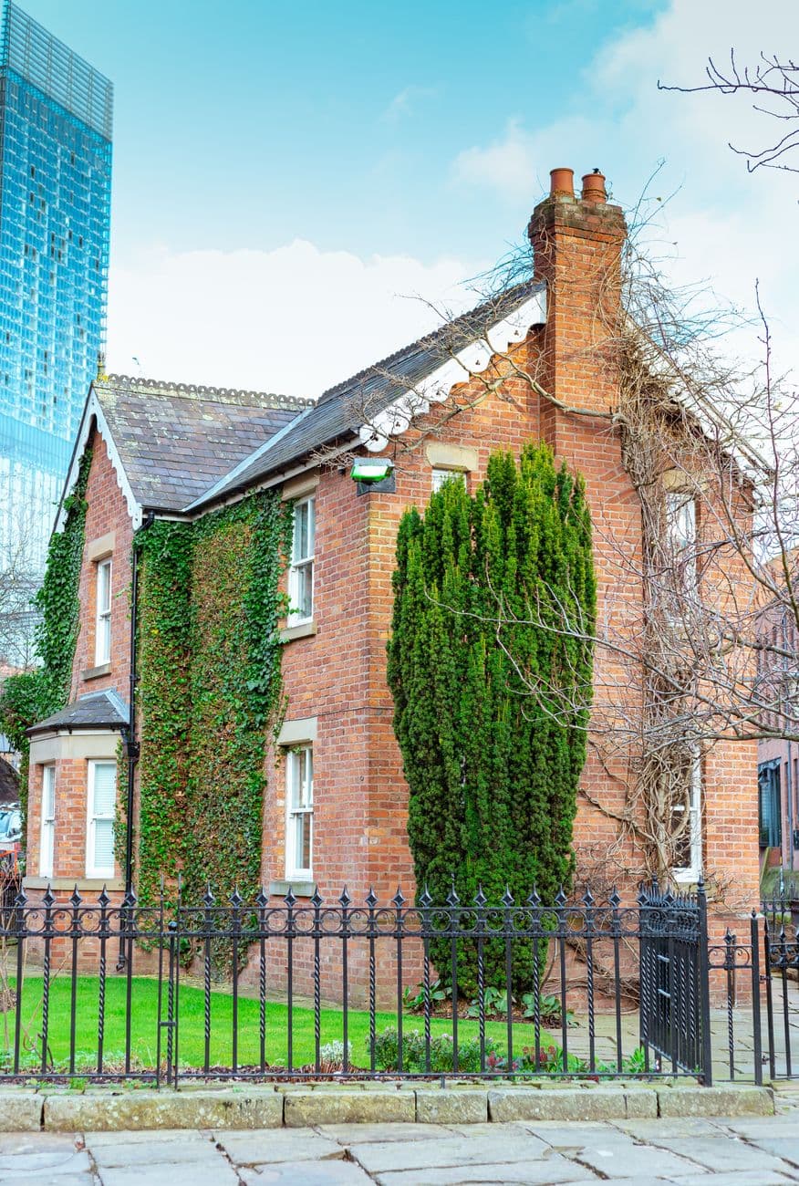 A quaint Victorian-style brick house in Manchester with ivy-covered walls and city skyscra