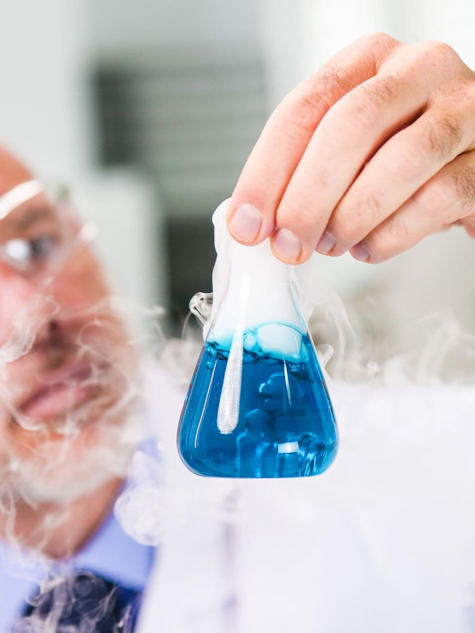 A scientist holding a flask with blue liquid and smoke during a lab experiment.