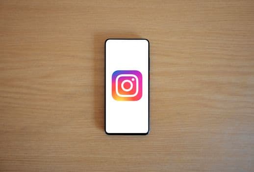 A smartphone with the Instagram logo on display, placed on a wooden surface. Perfect for t PNG
