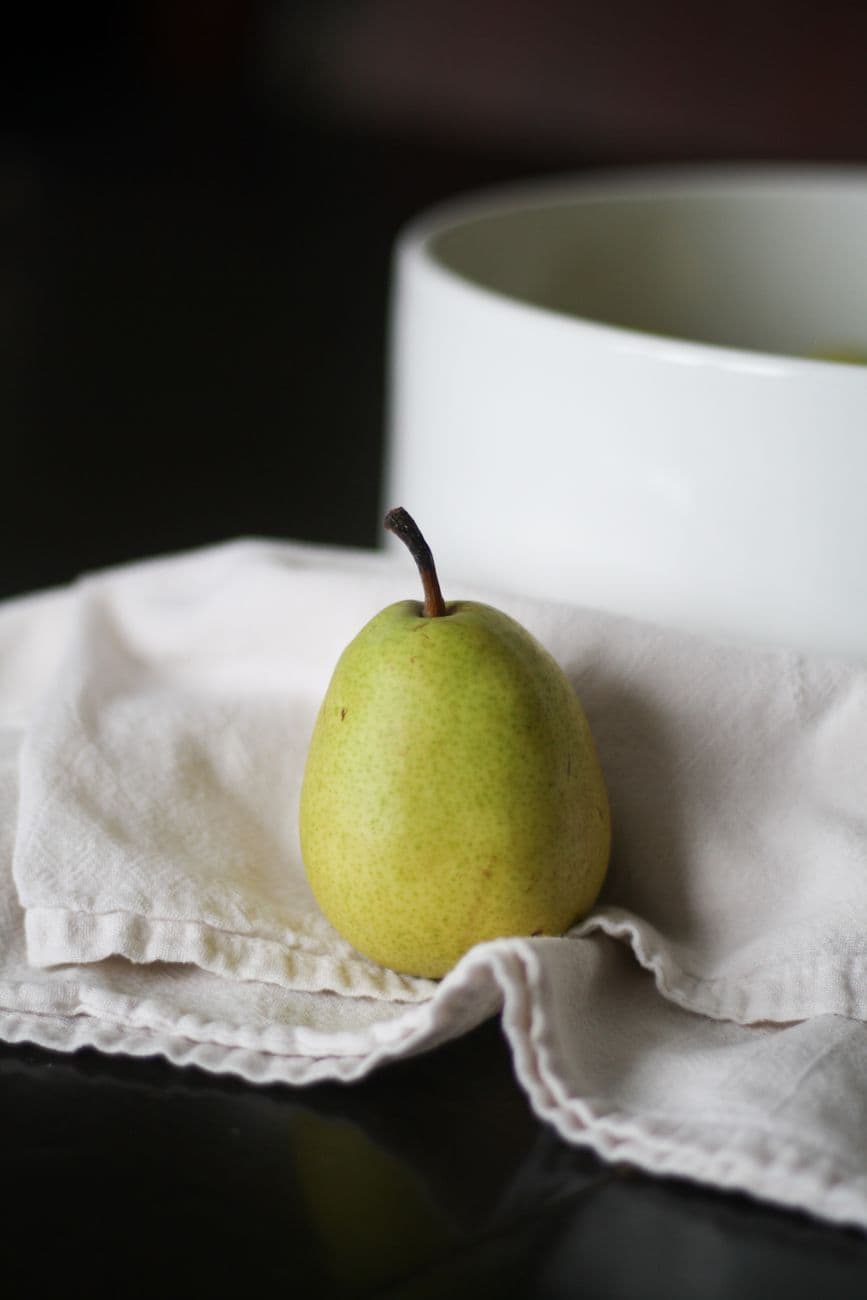 A vibrant green pear rests on a white cloth, offering a fresh and inviting look.