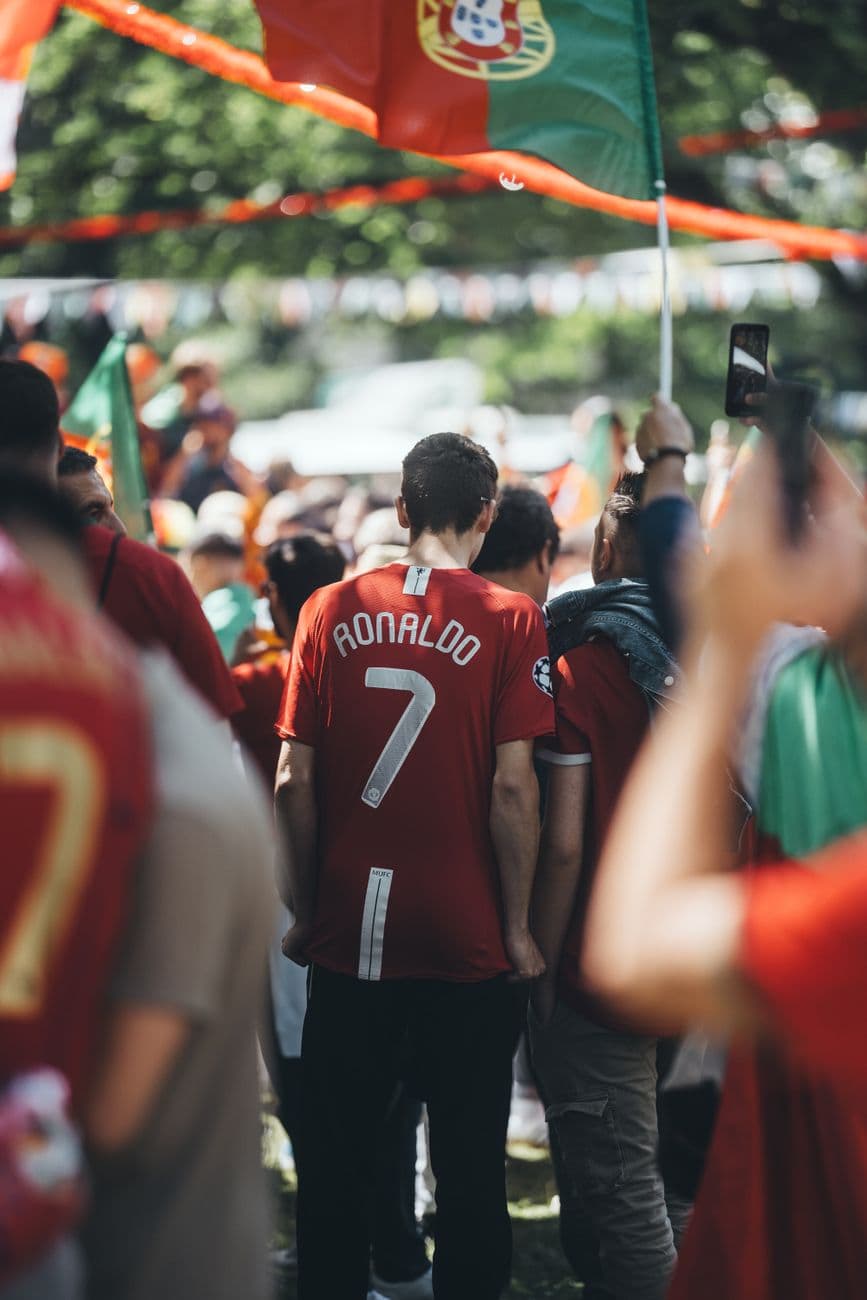 A vibrant outdoor scene of enthusiastic soccer fans wearing jerseys and waving flags durin
