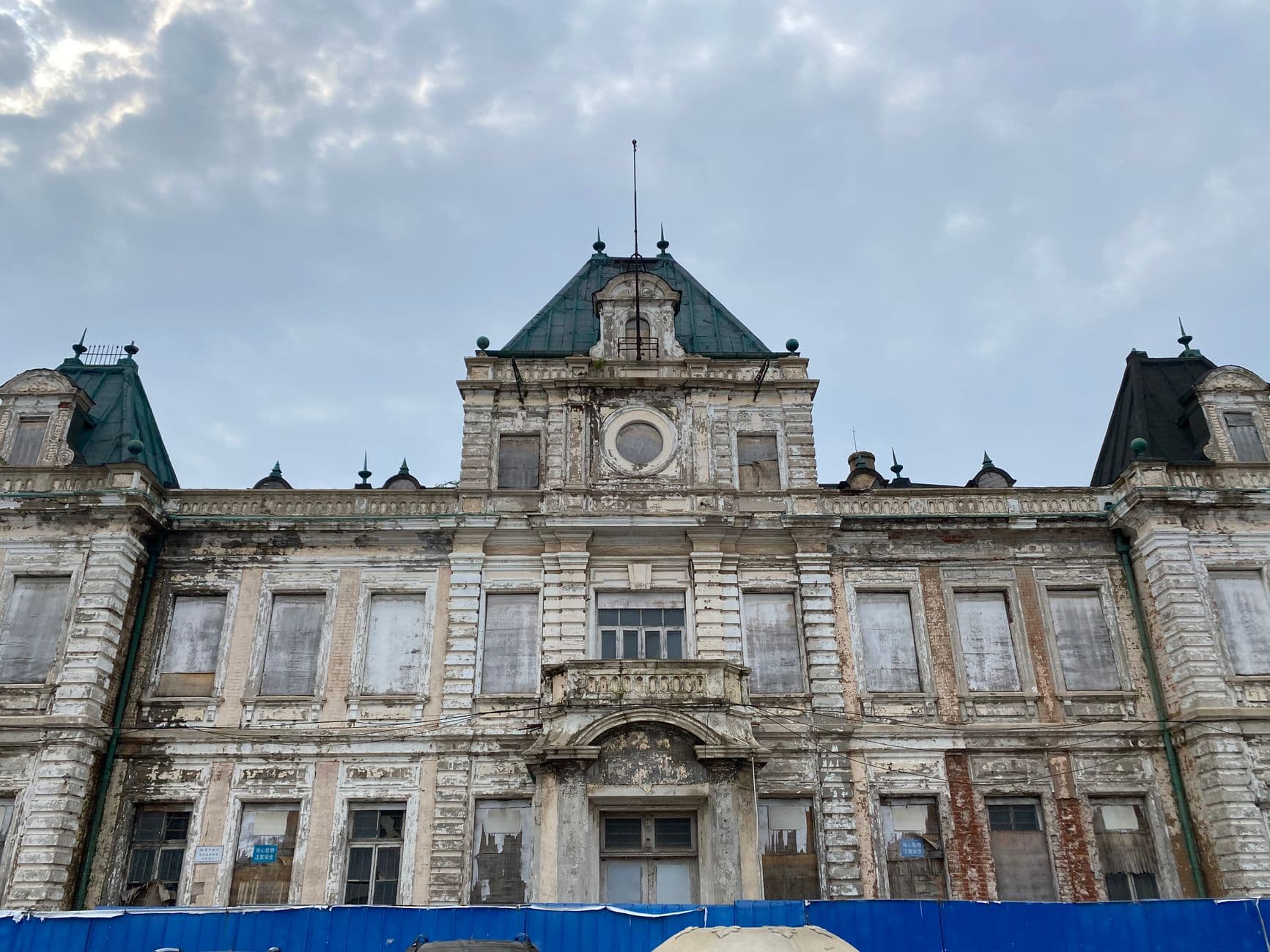 A weathered historical building with classic architecture stands against a cloudy sky, sho