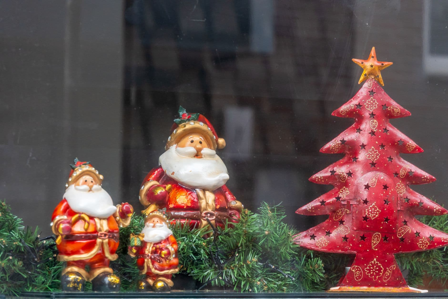 Adorable ceramic Santa Claus figurines beside a decorative red Christmas tree.
