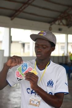 An adult man engaged in a card game indoors, holding colored playing cards. PNG
