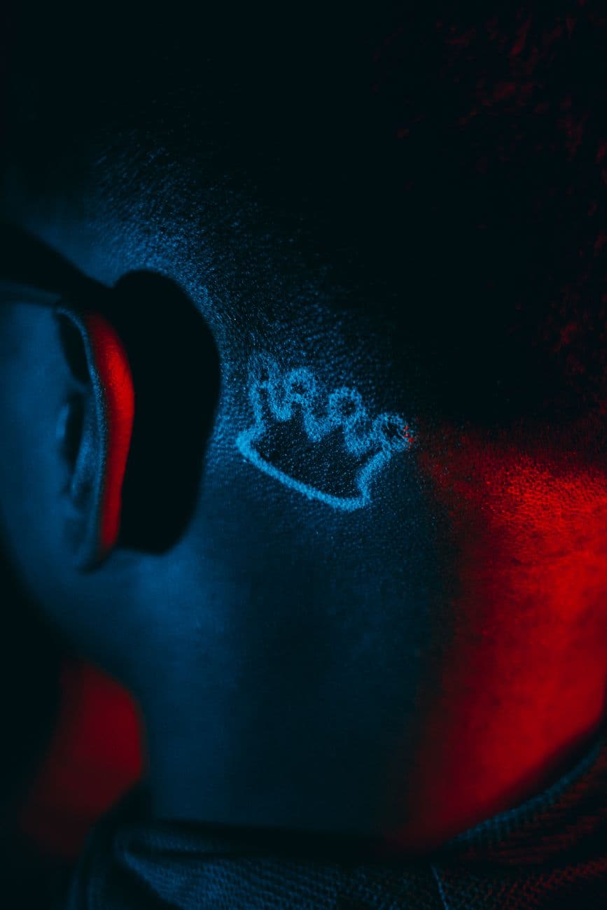 Artistic shot of a white ink tattoo shaped like a crown on a man's neck under dramatic lig