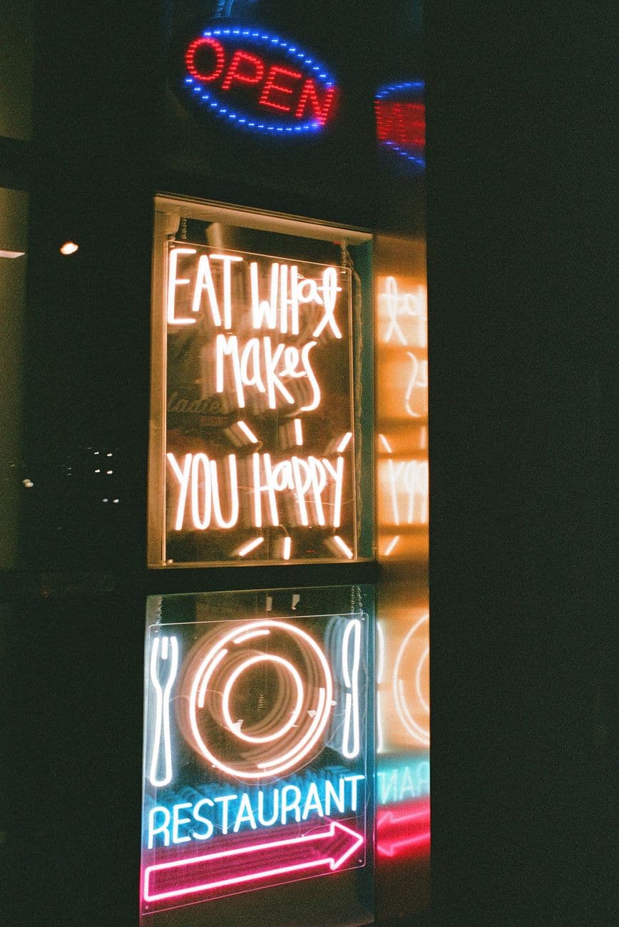 Bright neon restaurant signs with motivational text, captured with a film-like quality.