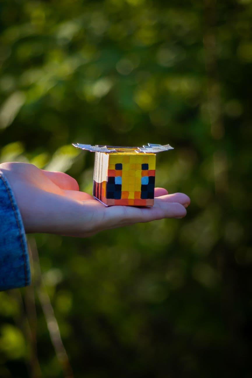 Close-up of a hand holding a Minecraft-inspired papercraft figurine outdoors.