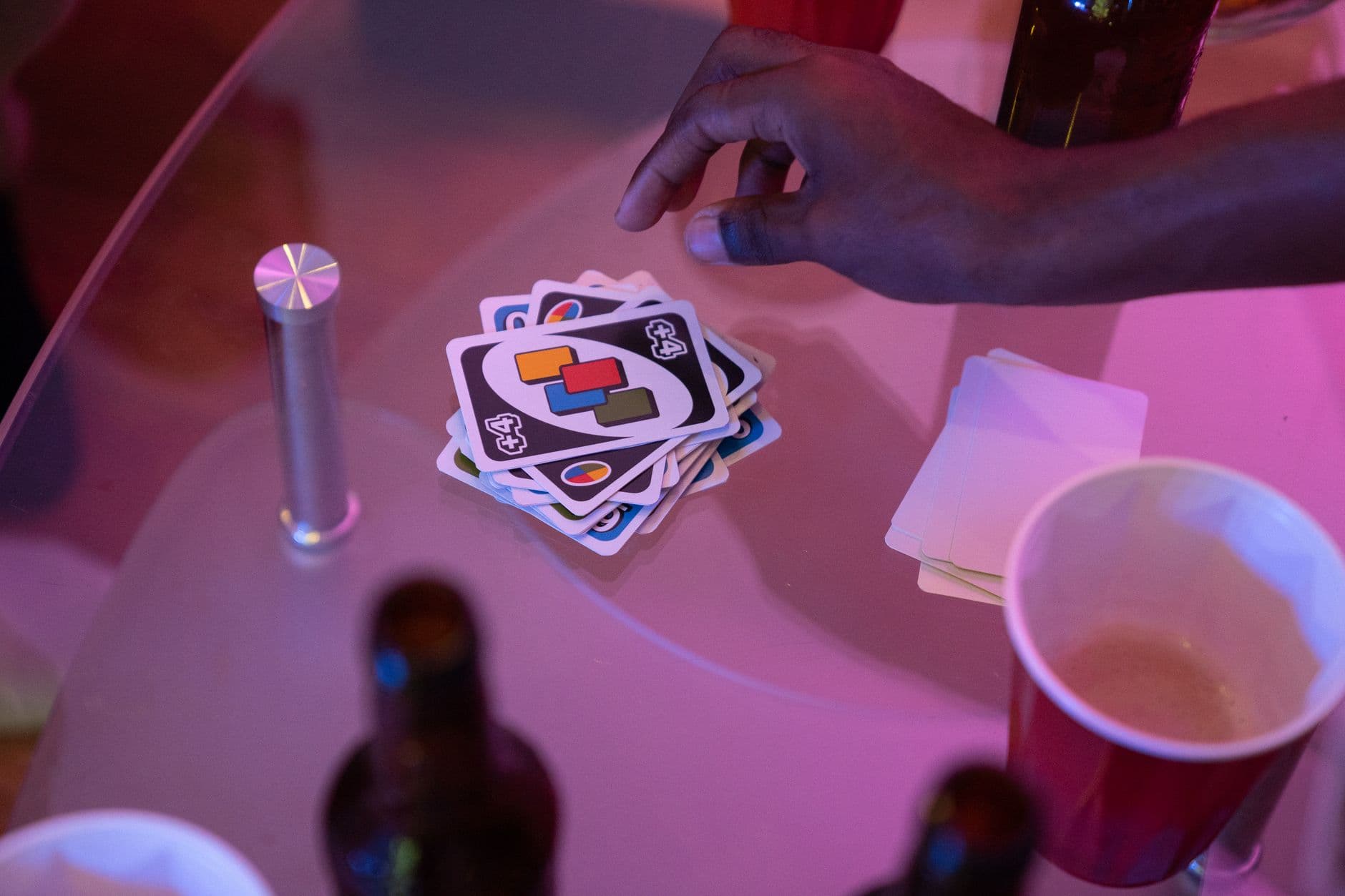 Close-up of a hand playing Uno cards on a table during a social gathering.
