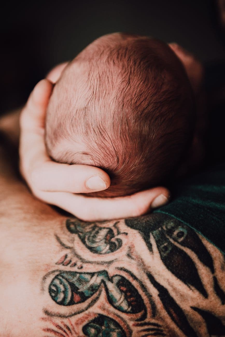 Close-up of a newborn cradled in tattooed arms, symbolizing love and protection.