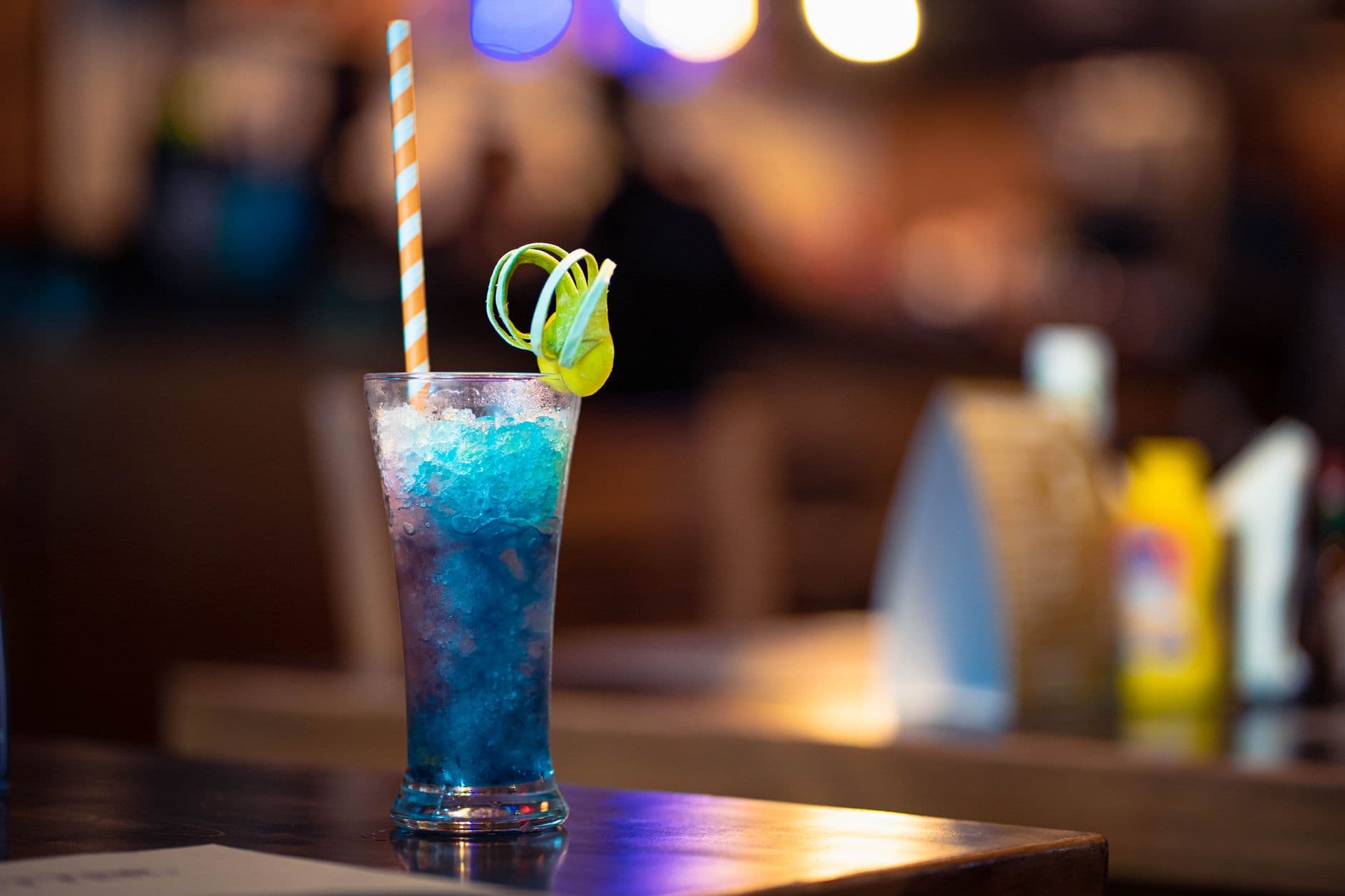 Close-up of a vibrant blue cocktail with citrus garnish on a bar table, perfect for nightl