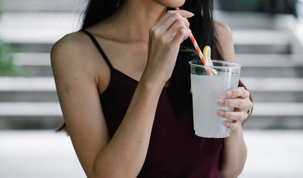 Close-up of a woman sipping refreshing lemonade with a striped straw outdoors. PNG