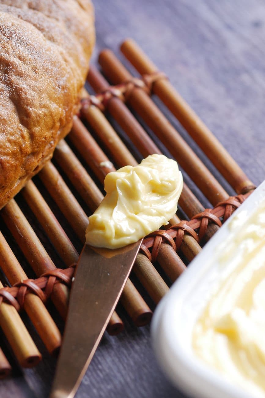 Close-up of butter spread on knife next to fresh bread on rustic mat, perfect for culinary