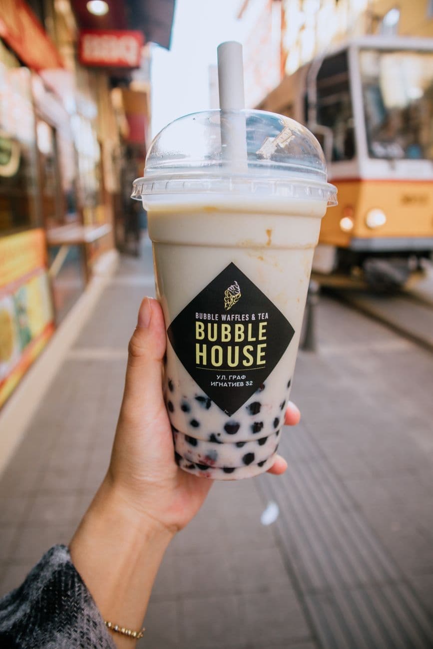 Close-up of hand holding bubble tea with city street background, featuring tram.