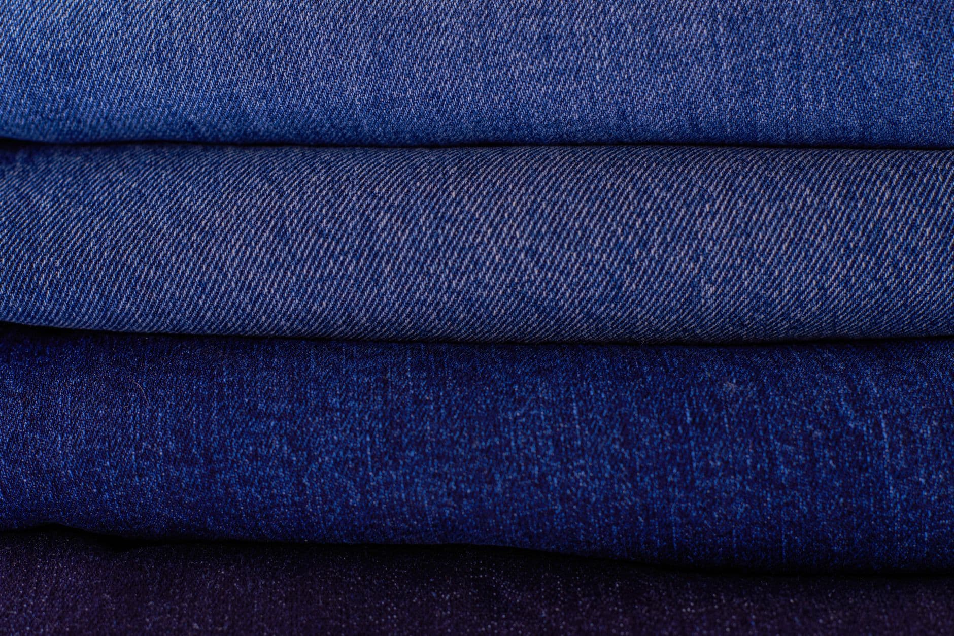 Close-up of neatly stacked folded denim fabrics in varying blue tones showcasing texture a