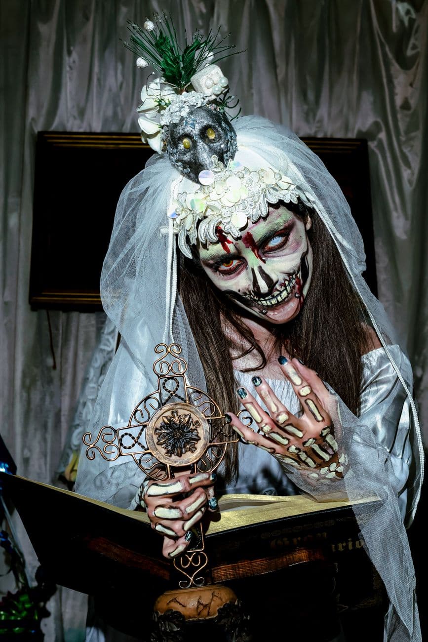 Creepy bride with skull makeup holding ornate cross, perfect for Halloween themes.