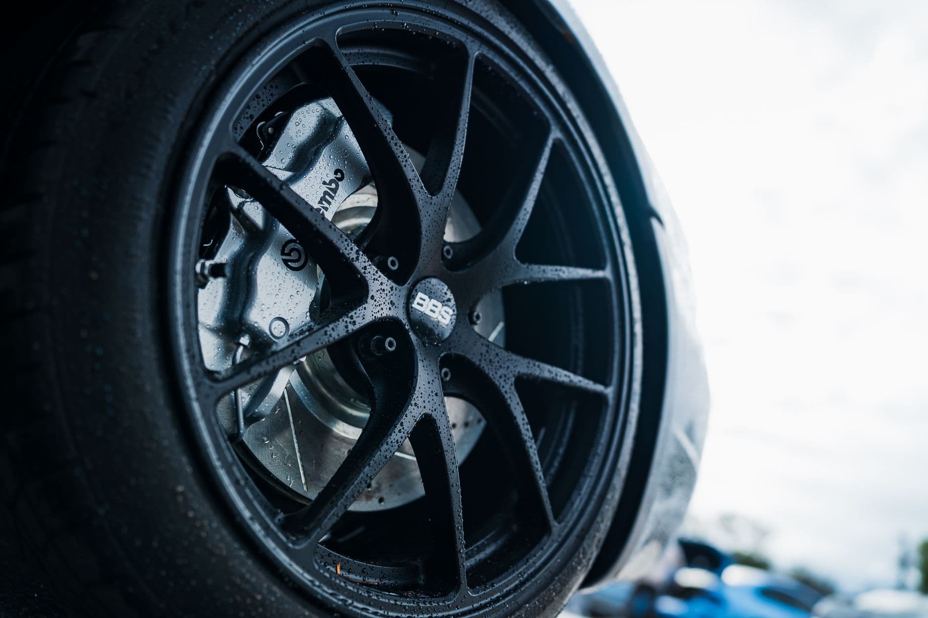 Detailed close-up of BBS car wheel showcasing Brembo brakes, outdoors in a rainy setting.