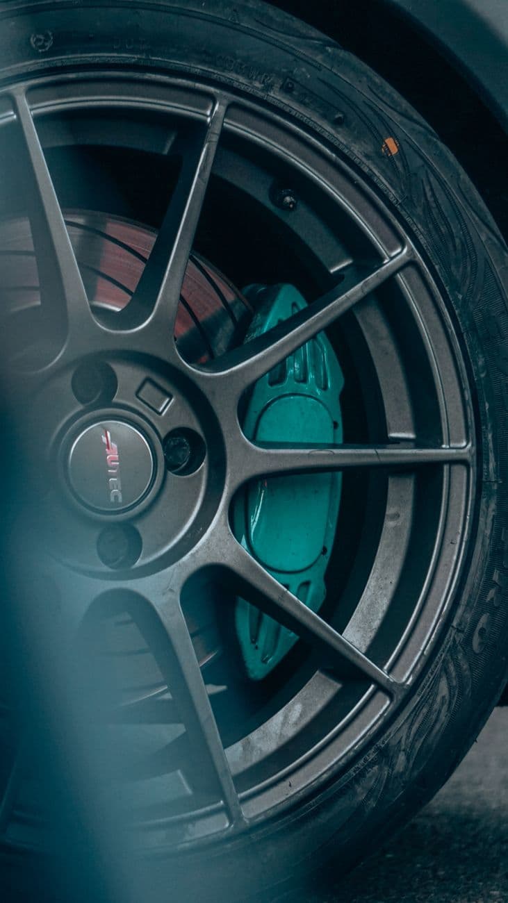 Detailed view of a car's alloy wheel and turquoise brake pads, emphasizing design and perf