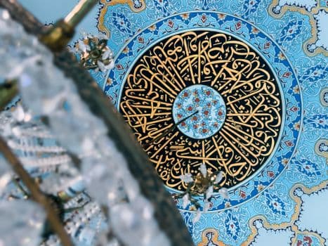 Detailed view of a mosque ceiling featuring elaborate Arabic calligraphy and blue geometri PNG